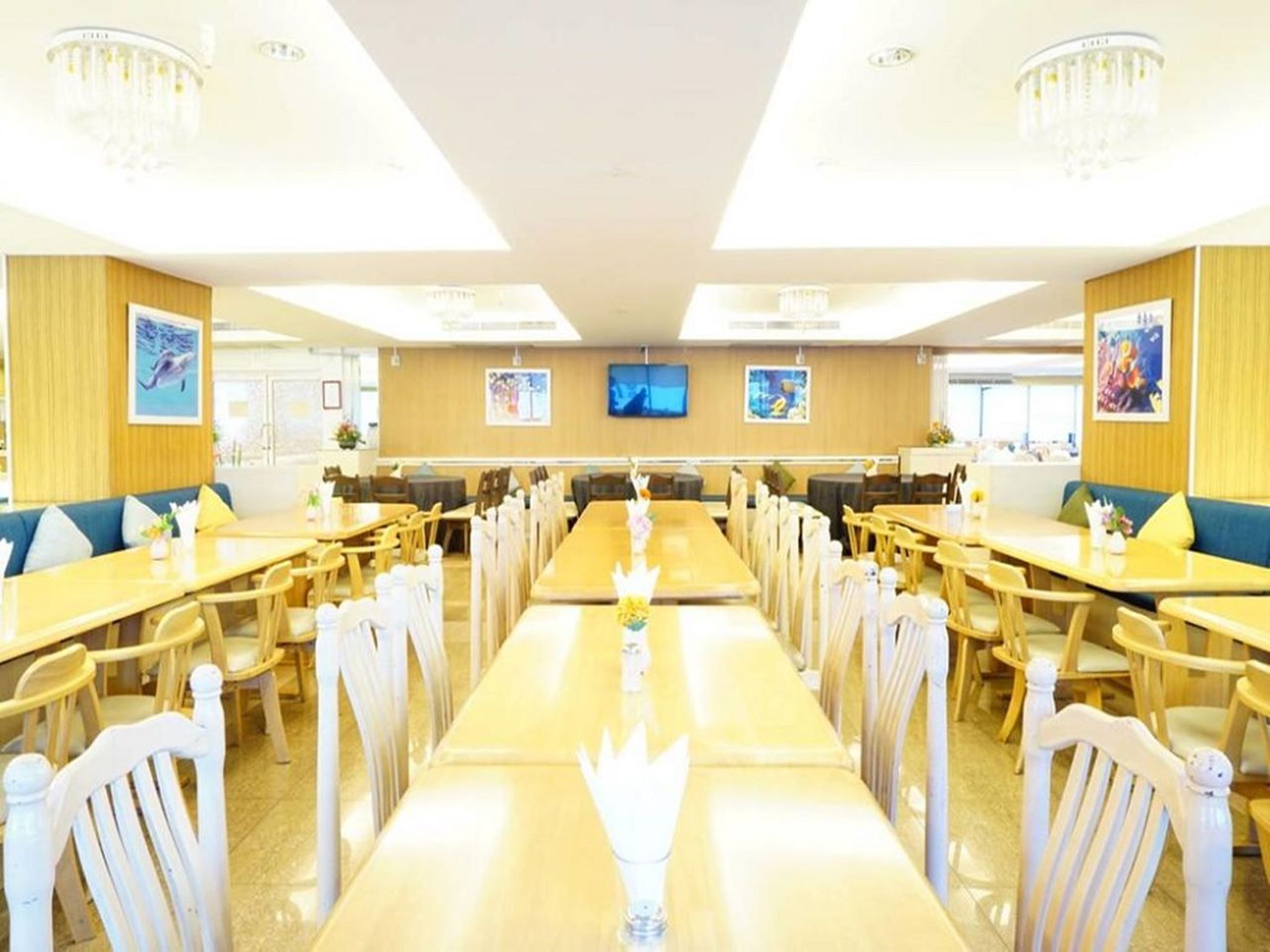A spacious dining area with long tables and chairs, wooden paneling, and chandeliers.