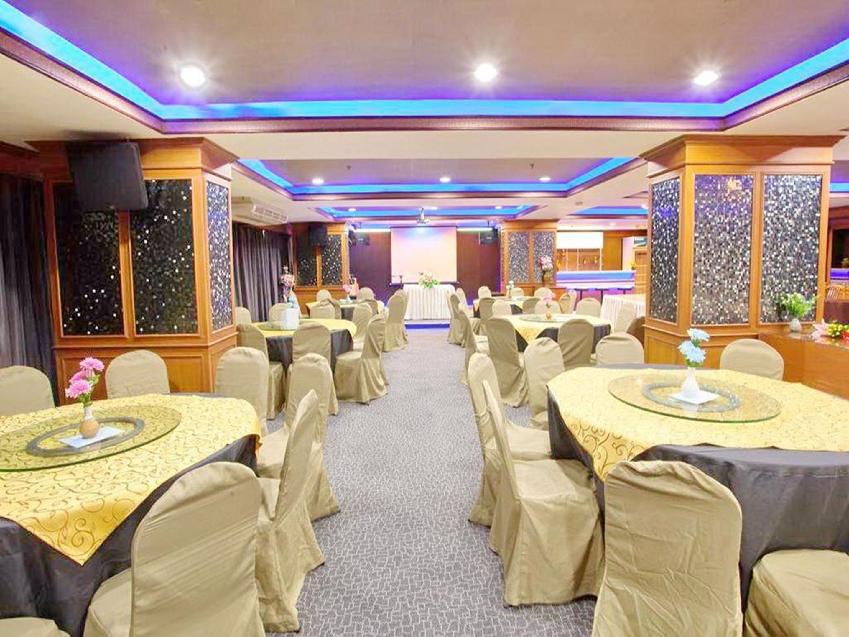 A banquet hall with round tables, chairs, and a stage.