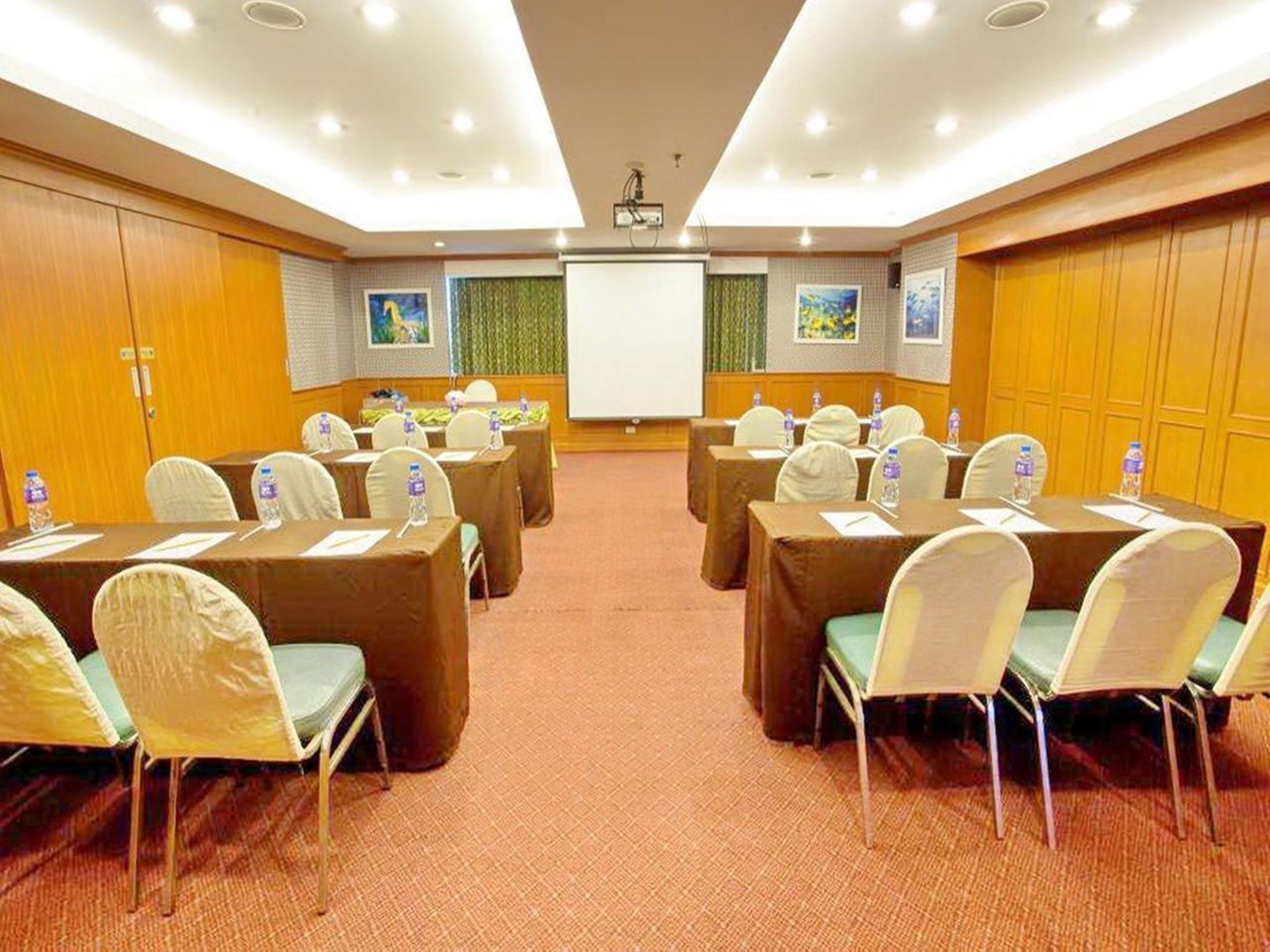 A conference room with tables, chairs, and a projector screen.
