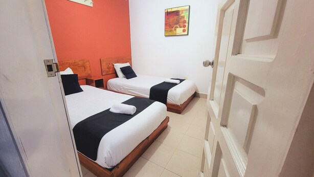 Habitació d'hotel amb dos llits, una paret vermella decorativa, un quadre i una porta blanca.