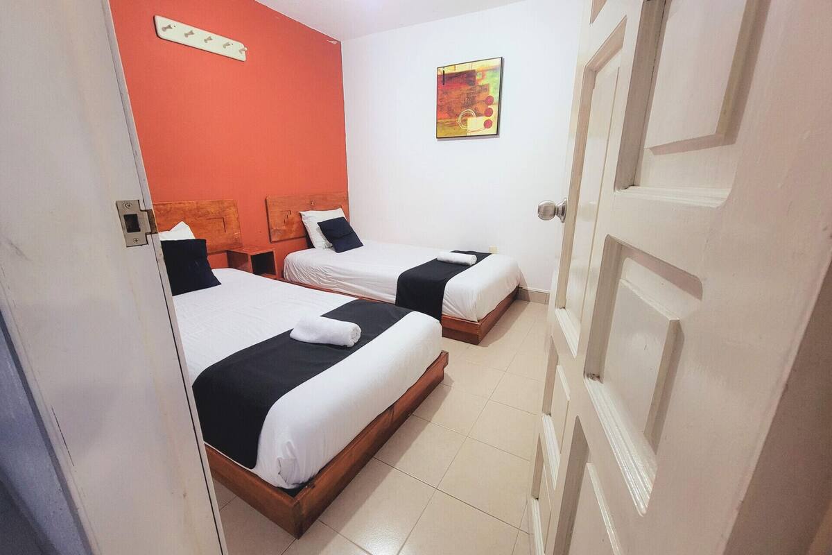 A hotel room with two beds, a red accent wall, a painting, and a white door.