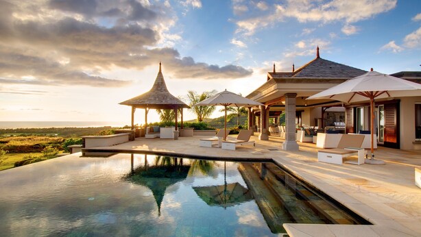 A luxurious outdoor pool area with a gazebo, lounge chairs, and umbrellas.