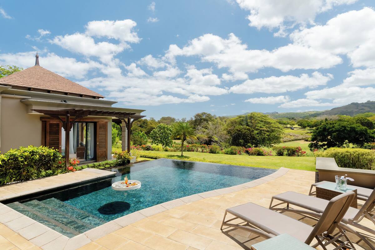 Une piscine dotée de chaises longues et d’une pergola, entourée d’un jardin aménagé et avec des collines en arrière-plan.