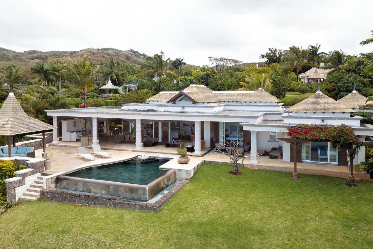 Une grande maison avec une piscine, un espace salon extérieur et une vue sur les collines.