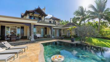 A luxurious house with a swimming pool, outdoor furniture, and tropical landscaping.
