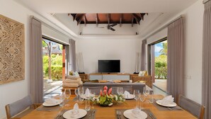 A dining area with a wooden table set for a meal, a television in the background, and a view of the outdoors.