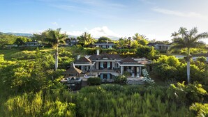 A large, multi-story house surrounded by lush greenery and palm trees.