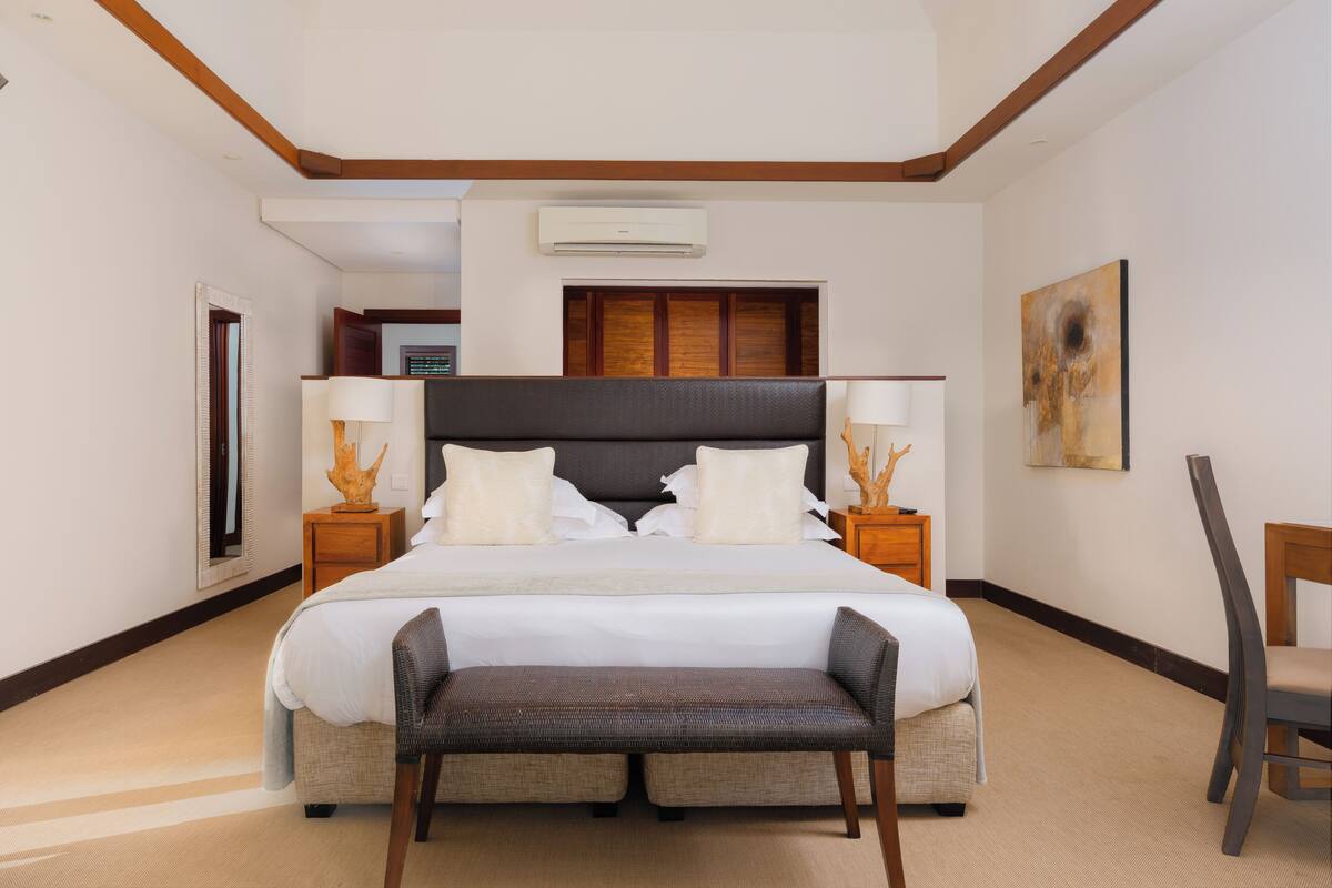 Une chambre d’hôtel avec un grand lit, deux tables de chevet avec des lampes, un banc, une chaise et un tableau au mur.