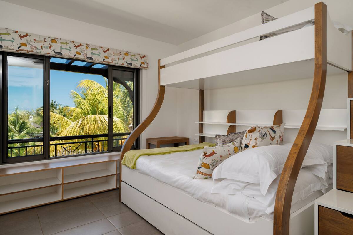 Un lit superposé avec vue sur les palmiers, visible à travers une grande fenêtre.
