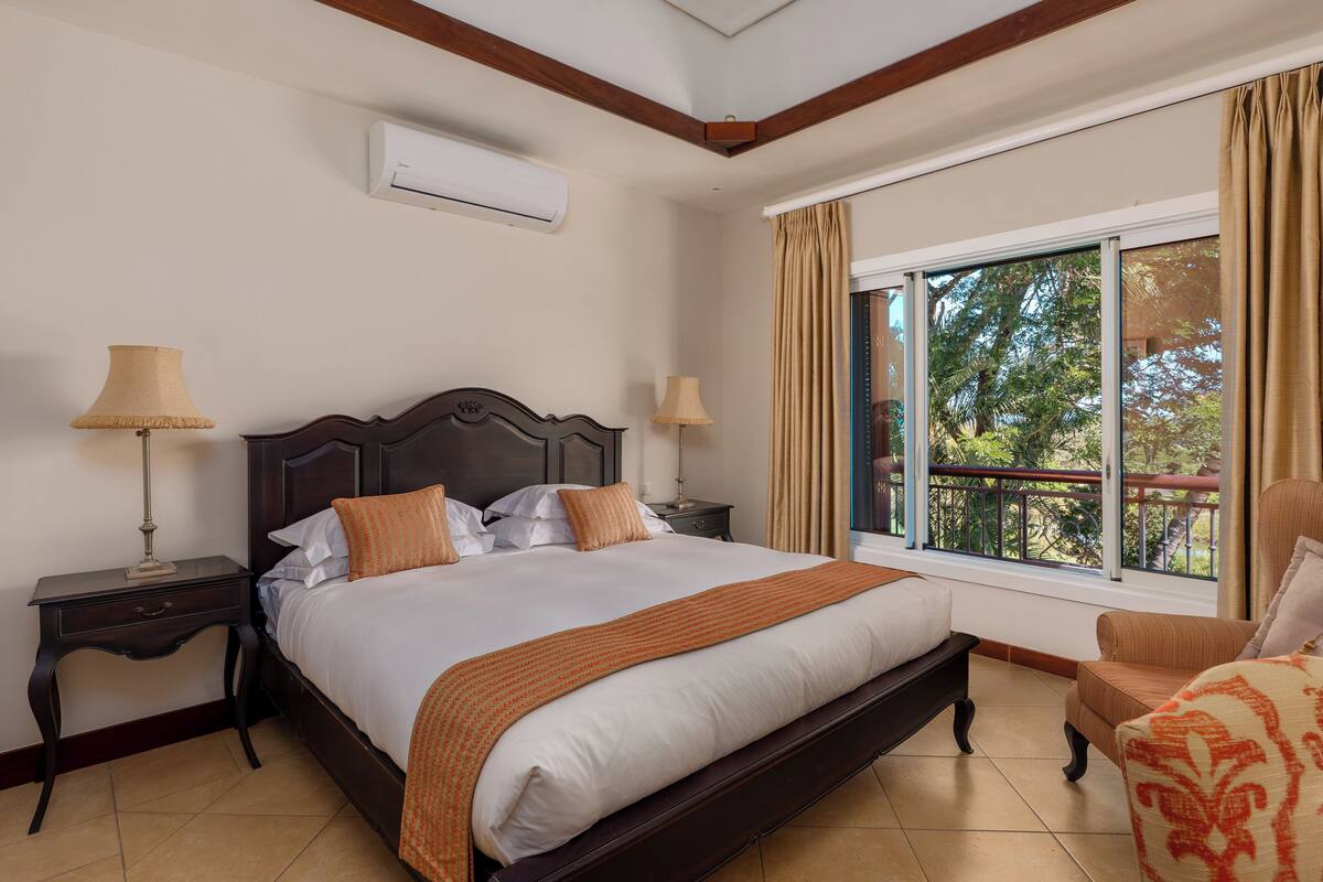 Une chambre d’hôtel avec un grand lit, deux tables de chevet, une fenêtre avec des rideaux et un balcon.