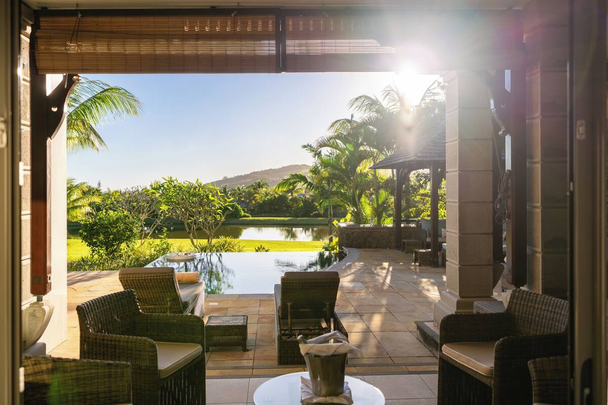 Un espace extérieur aménagé avec des meubles en osier, une petite piscine et une vue sur un jardin paysager et des collines.