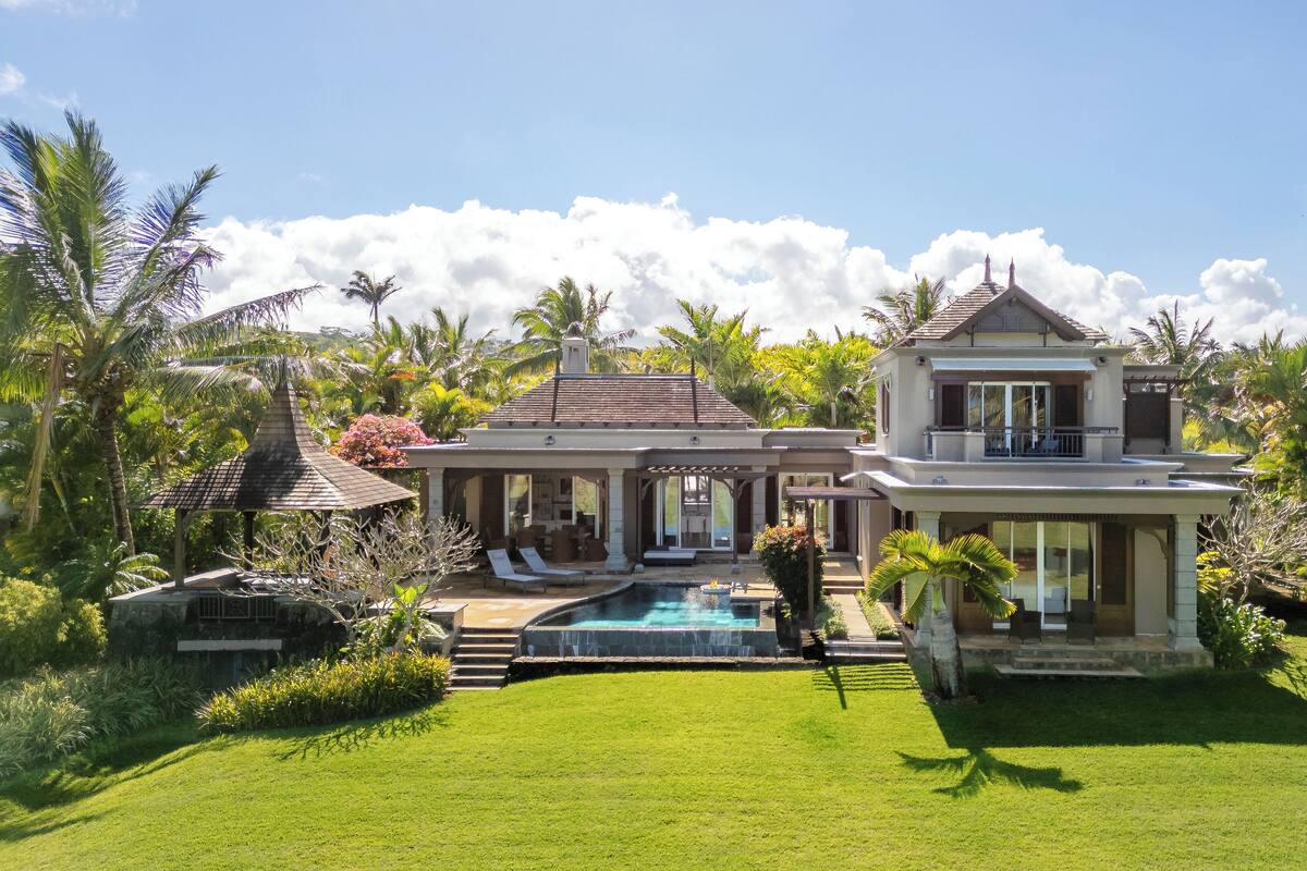 Une maison à deux étages dotée d’une piscine, d’un patio couvert et d’une végétation luxuriante.