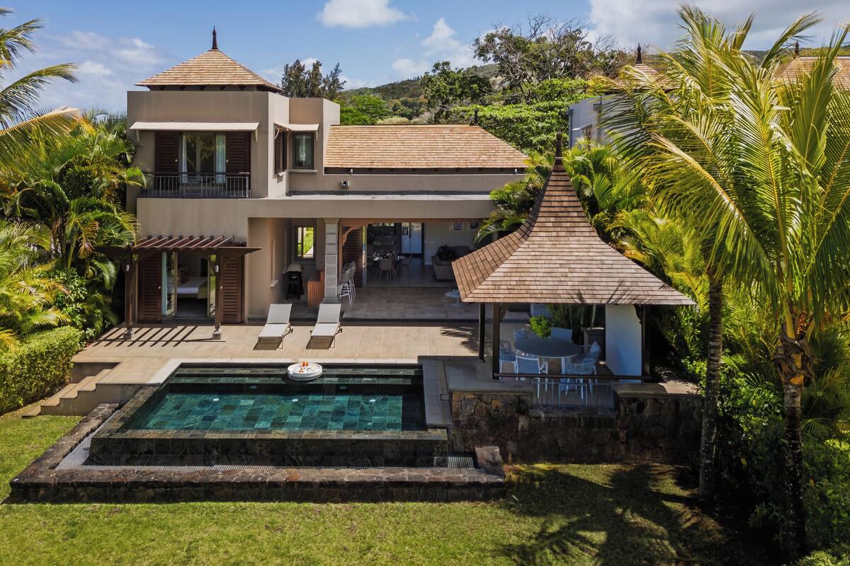 Une maison à deux étages avec une piscine, un patio doté de chaises et un espace extérieur couvert.