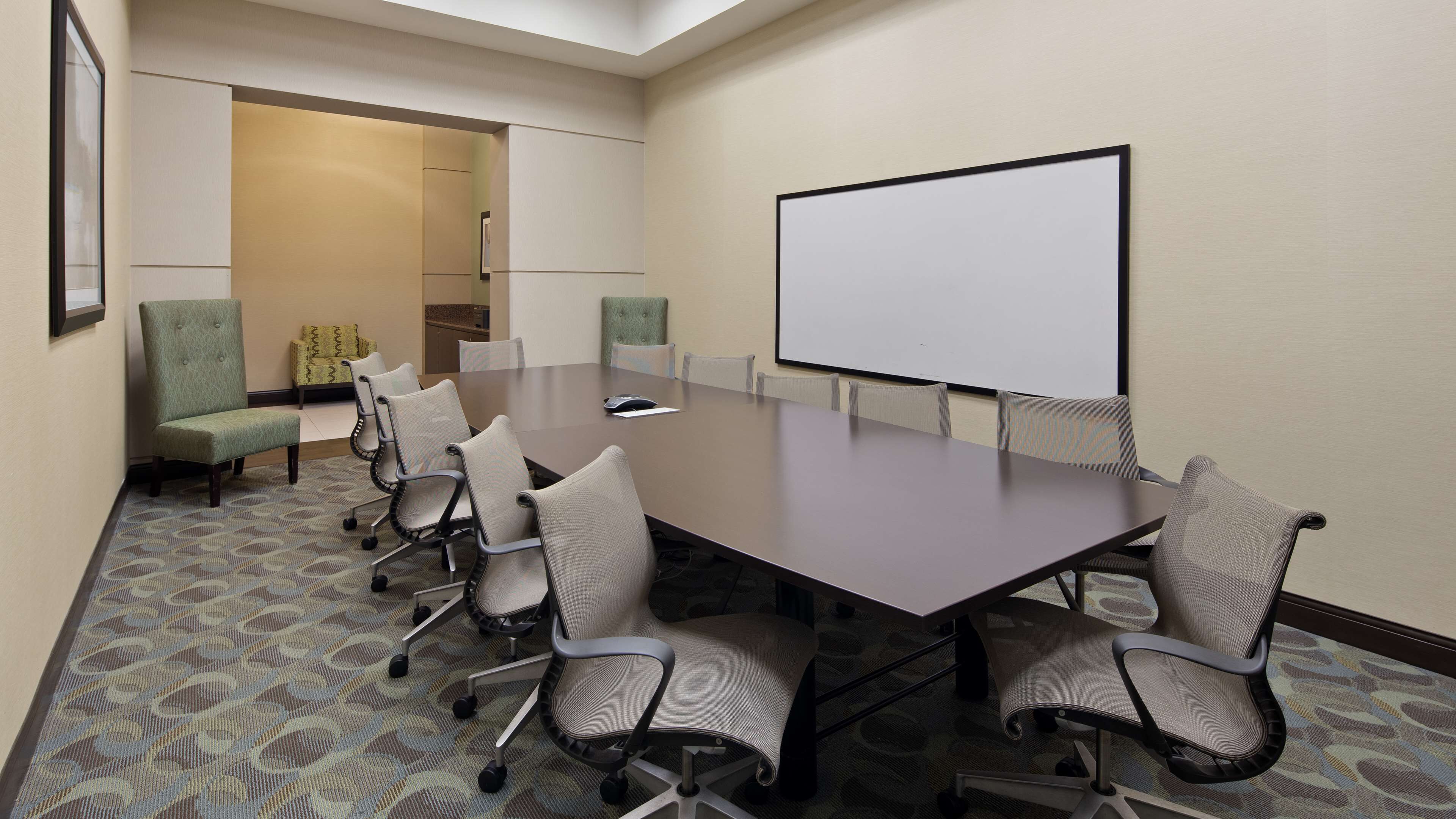 Une salle de conférence avec une longue table, six chaises, un écran de projection et un sol recouvert de moquette.