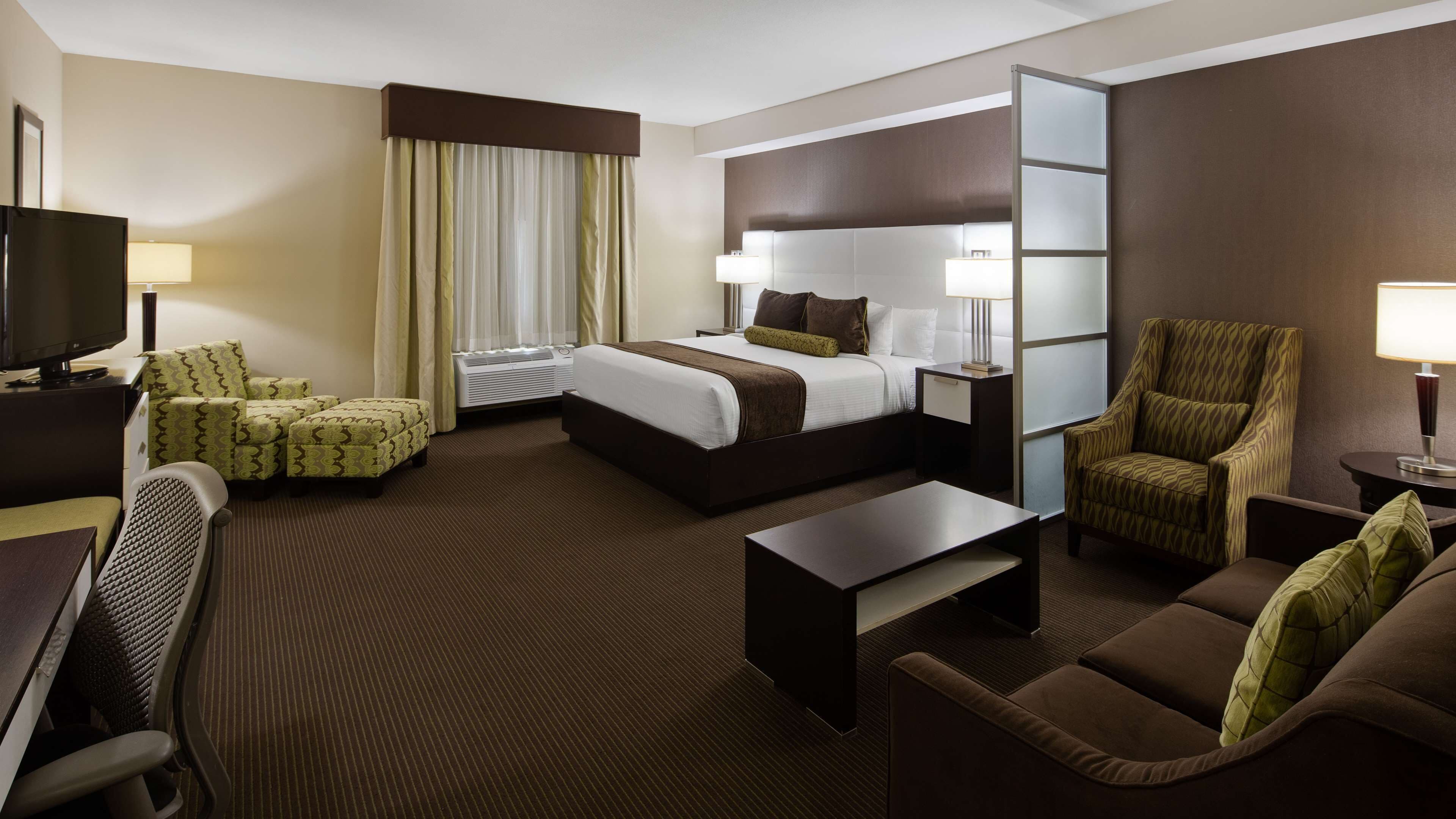 A hotel room with a bed, two armchairs, a sofa, a desk, a TV, and a lamp.