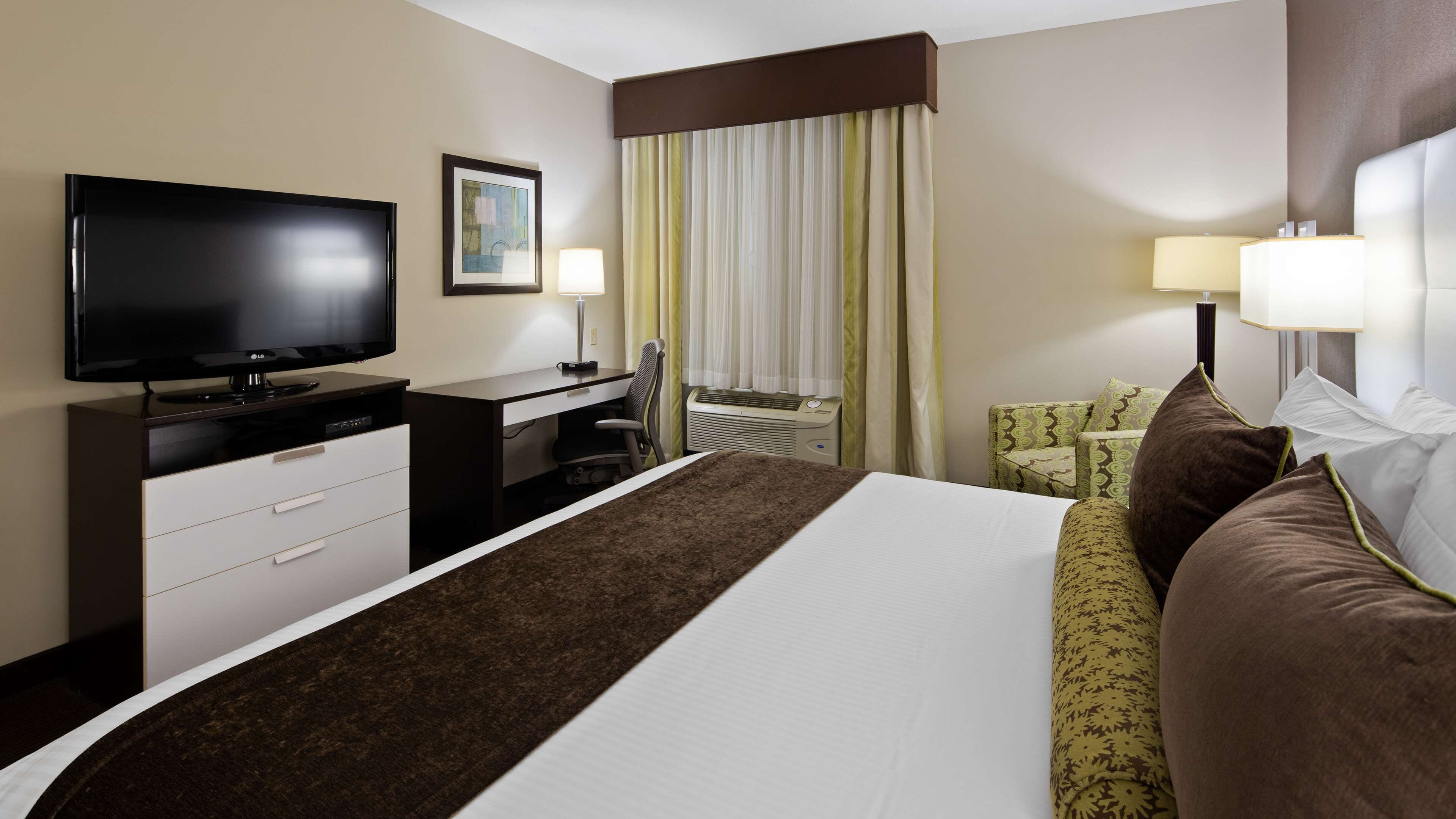 Ein Hotelzimmer mit Bett, Schreibtisch mit Fernseher, Stuhl, Lampe und einem Fenster mit Vorhängen.