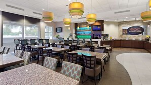 A restaurant with multiple tables and chairs, a bar area, and a large screen displaying a menu. - Best Western Plus Miami Intl Airport Hotel & Suites Coral Gables (Miami)