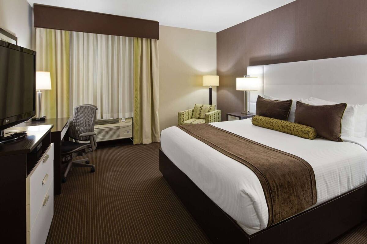 A hotel room with a large bed, a desk with a chair, a TV, and two bedside lamps.