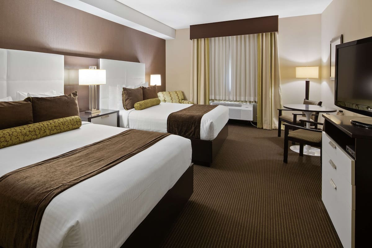 A hotel room with two beds, a desk, a television, and a window with curtains.