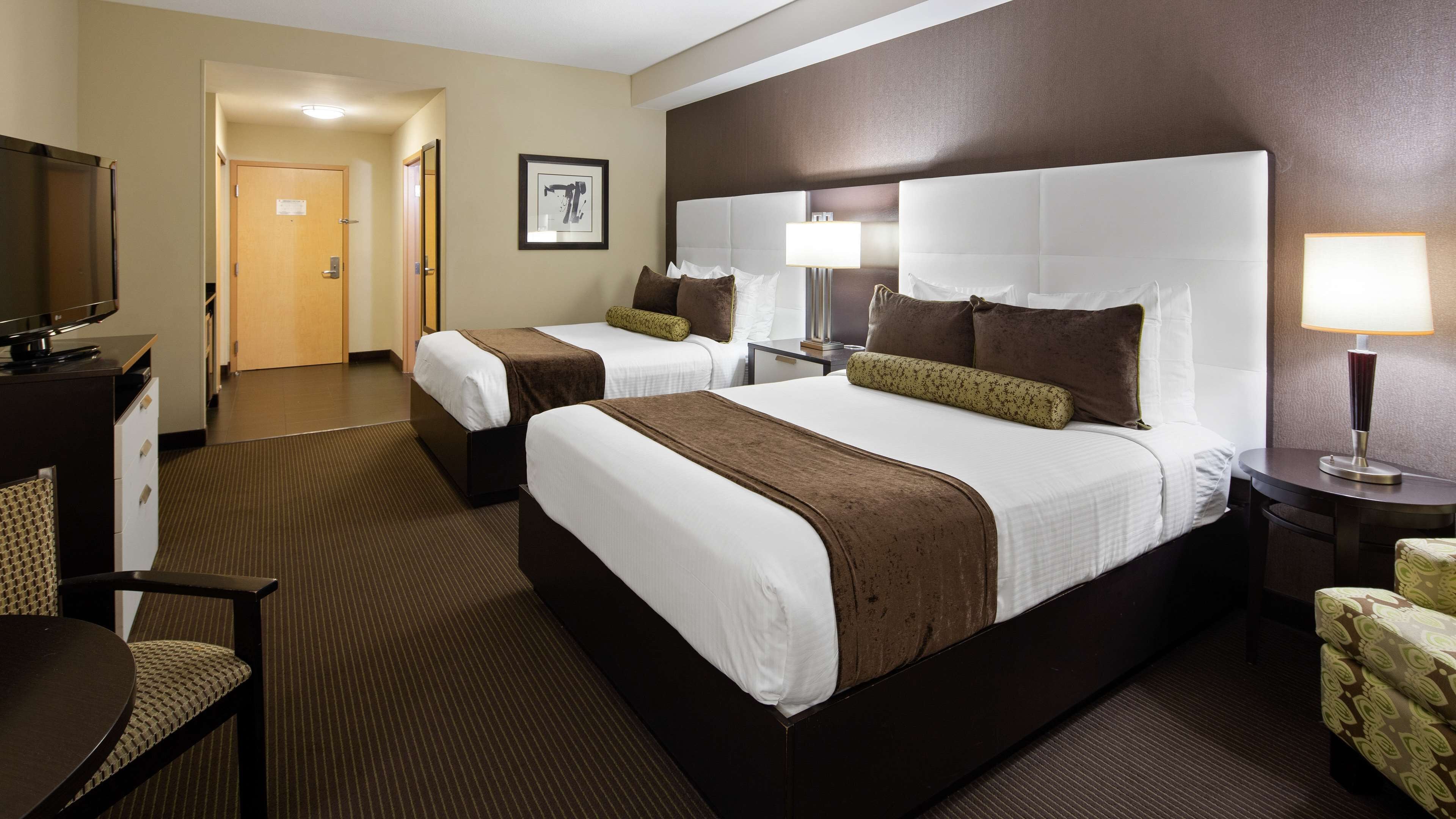 A hotel room with two beds, a TV, a desk, and a chair.