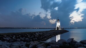 A lighthouse at a rocky shoreline with calm water reflecting the structure.