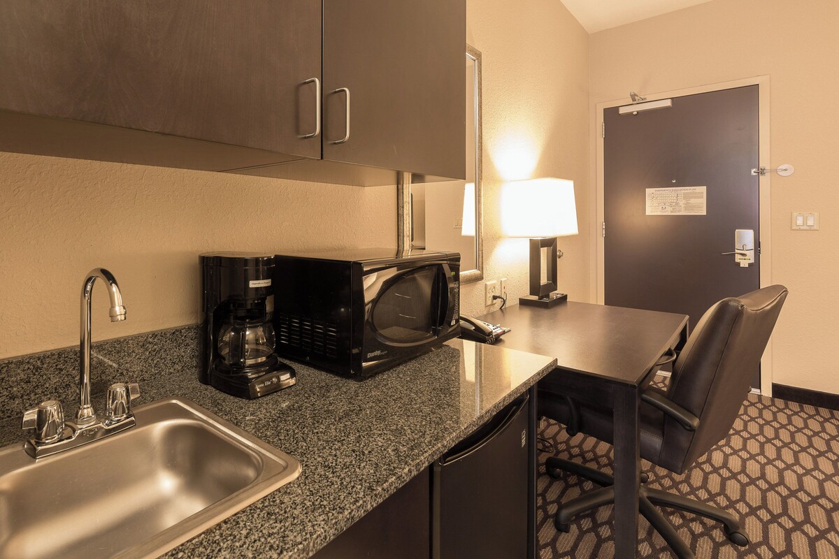 Una kitchenette de hotel con un lavamanos, una cafetera, un microondas y una silla.