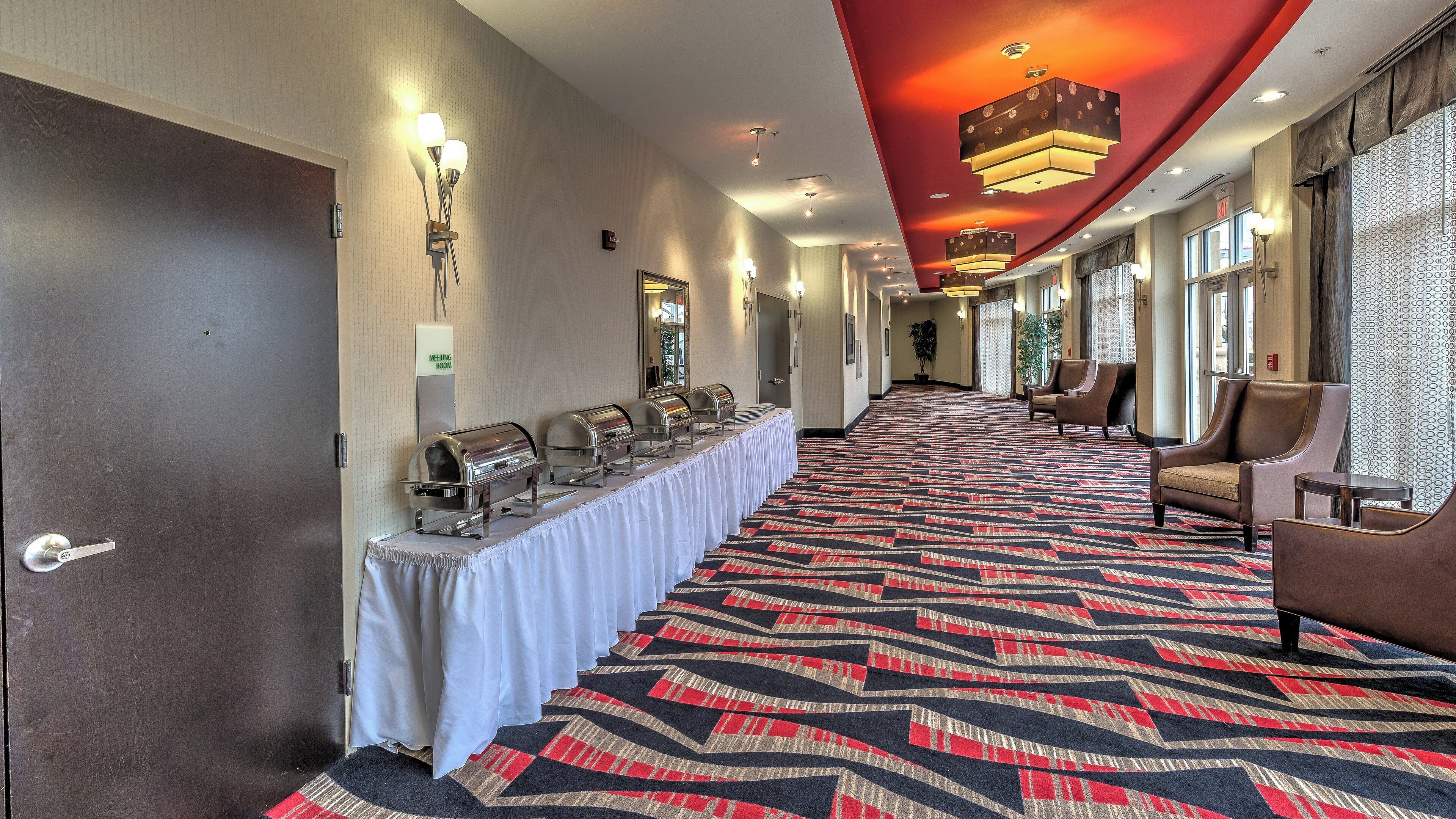 A hotel corridor with a buffet setup, seating area, and a meeting room sign.