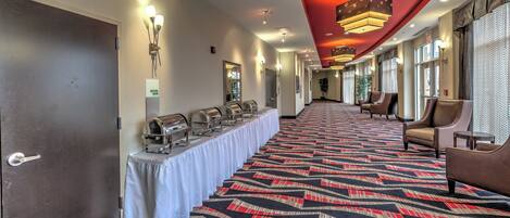 A hotel corridor with a buffet setup, seating area, and a meeting room sign.