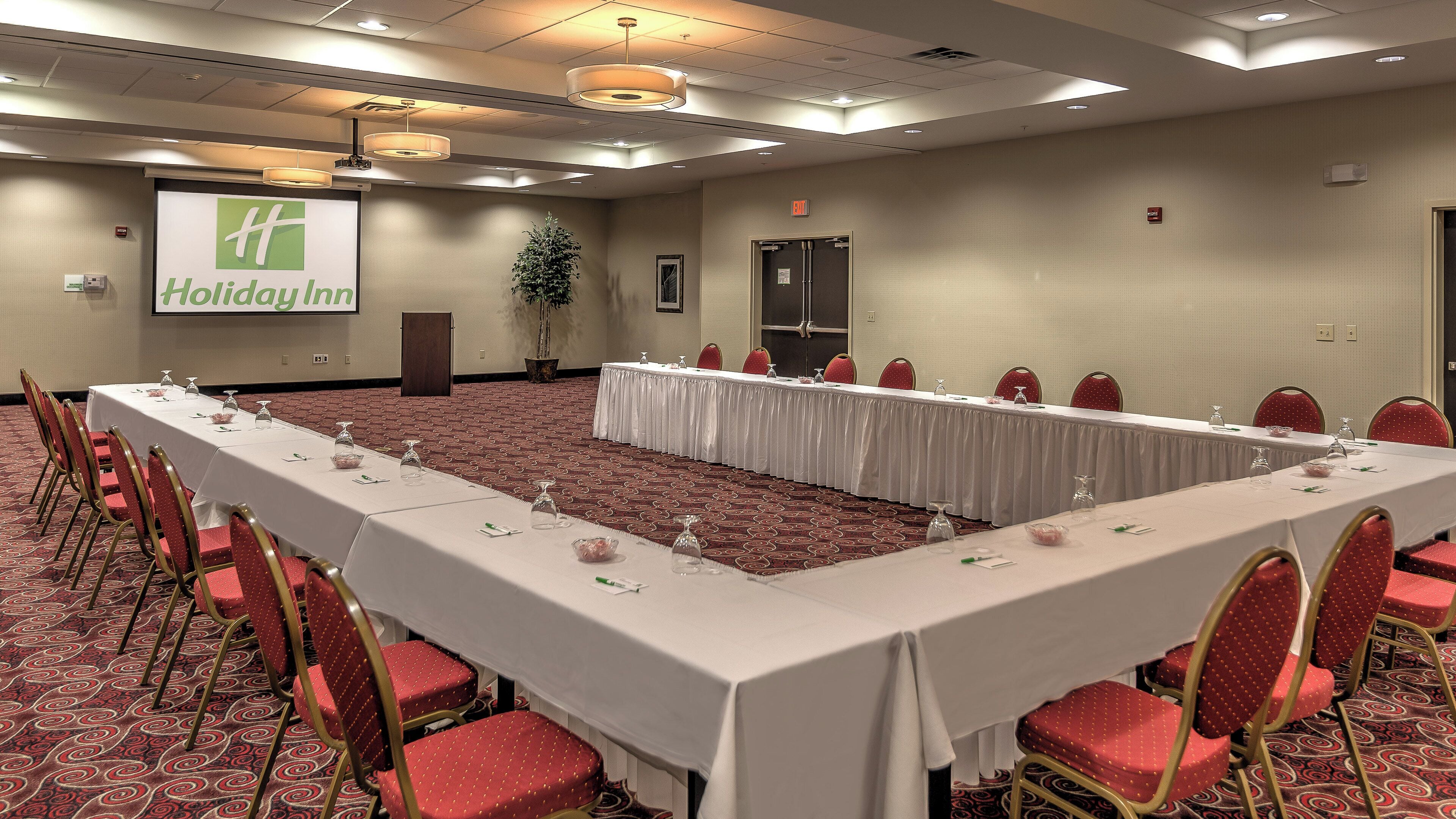 A conference room with a long table, red chairs, and a projector screen displaying 'Holiday Inn'.