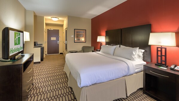 A hotel room with a bed, a desk with a computer, a chair, a lamp, and a television displaying the Holiday Inn logo.