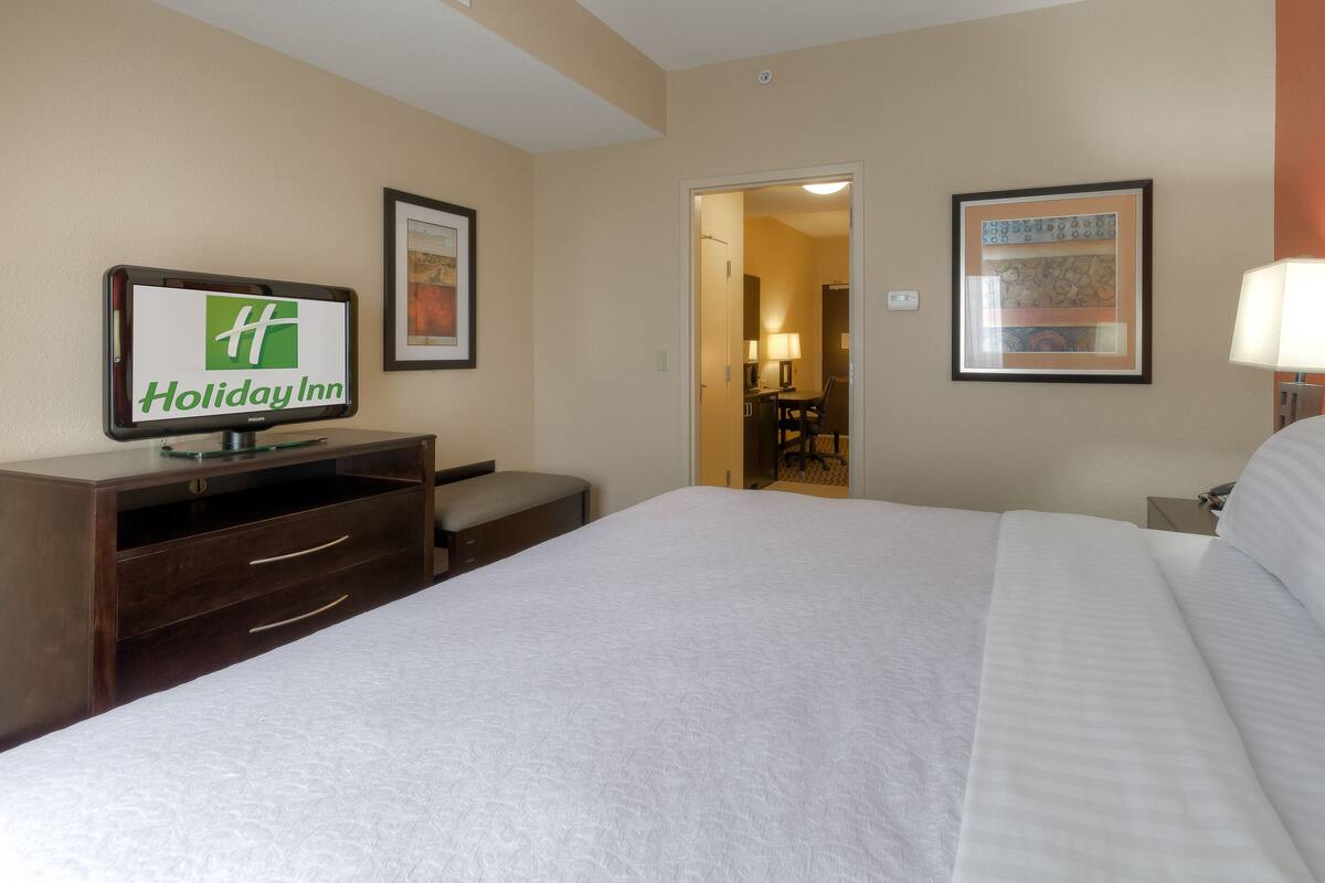 A hotel room with a bed, a desk with a computer, a chair, and a TV displaying the Holiday Inn logo.