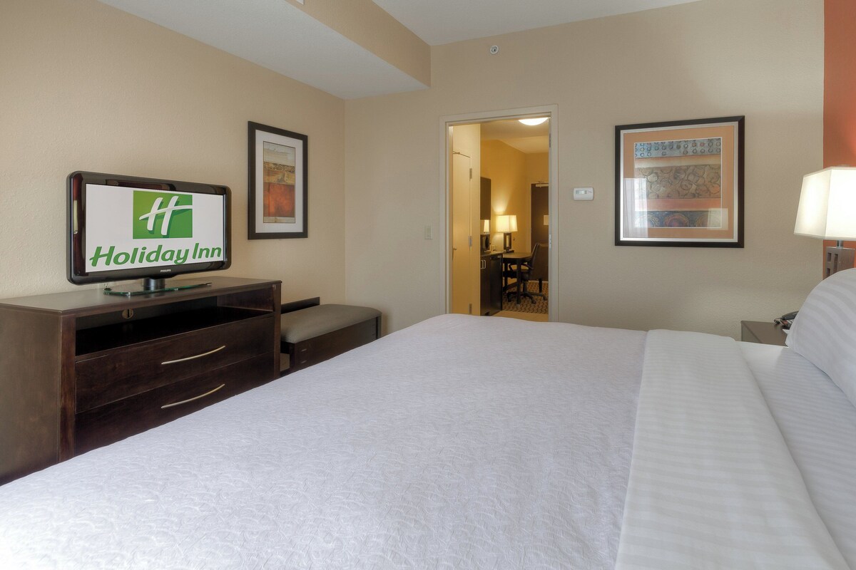 Una habitación de hotel con una cama, un escritorio, una silla y un televisor mostrando el logo de Holiday Inn.
