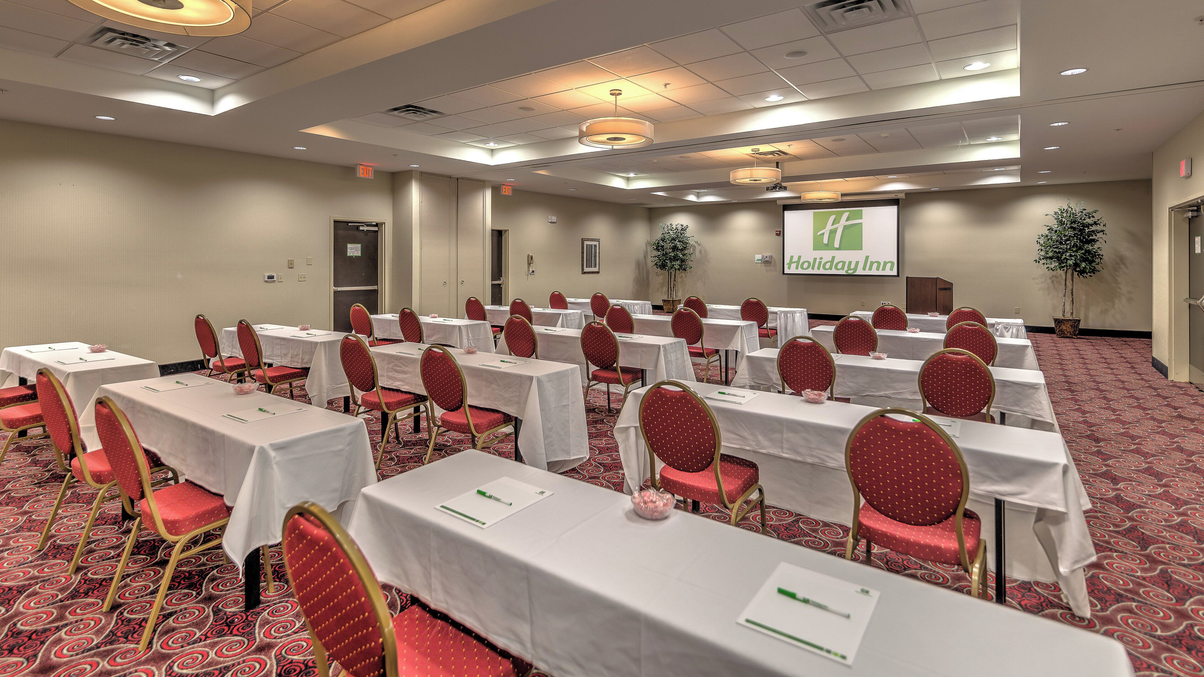 A conference room with tables and chairs, a projector screen, and a Holiday Inn sign.