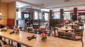 Restaurante de hotel con varias mesas para comer, sillas y una zona de cocina central.
