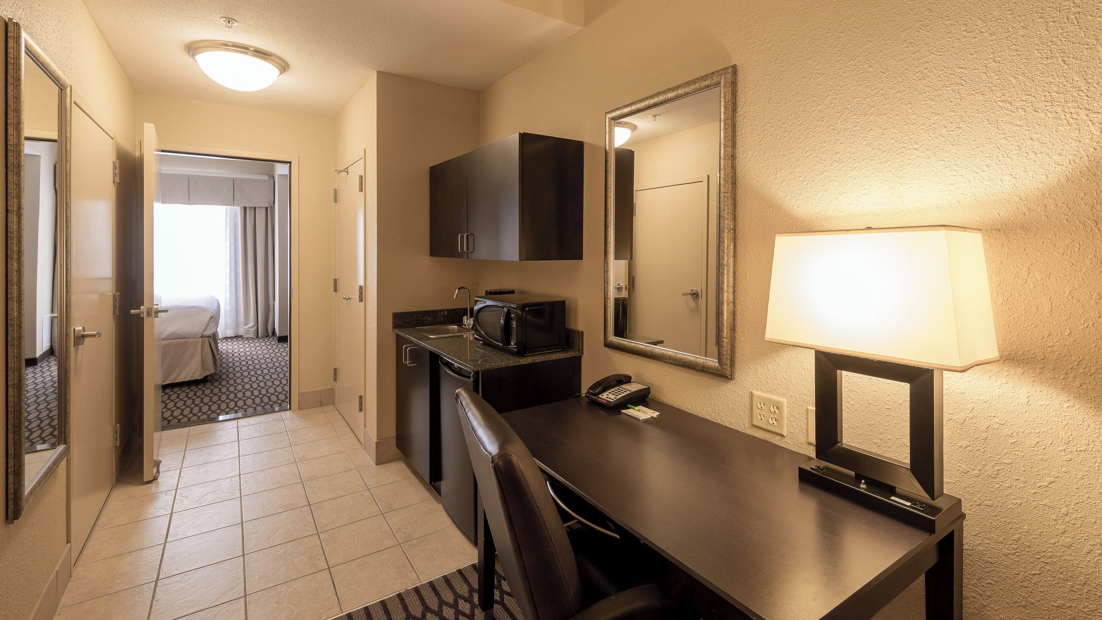 Une chambre d’hôtel équipée d’une kitchenette, d’un bureau, d’une chaise, d’un téléphone et d’un miroir.