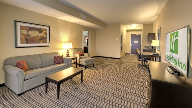 A hotel room with a sofa, armchair, coffee table, and a desk with a computer.