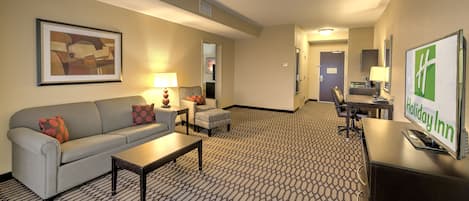 A hotel room with a sofa, armchair, coffee table, and a desk with a computer.