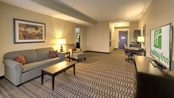 Habitación de hotel con sofá, sillón, mesita de café y escritorio con computadora.