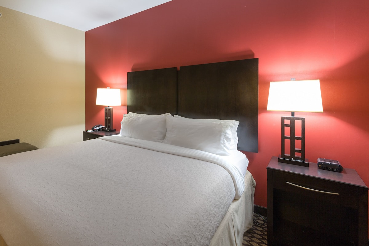 A hotel room with a large bed, two bedside tables with lamps, a framed picture on the wall, and a patterned floor.
