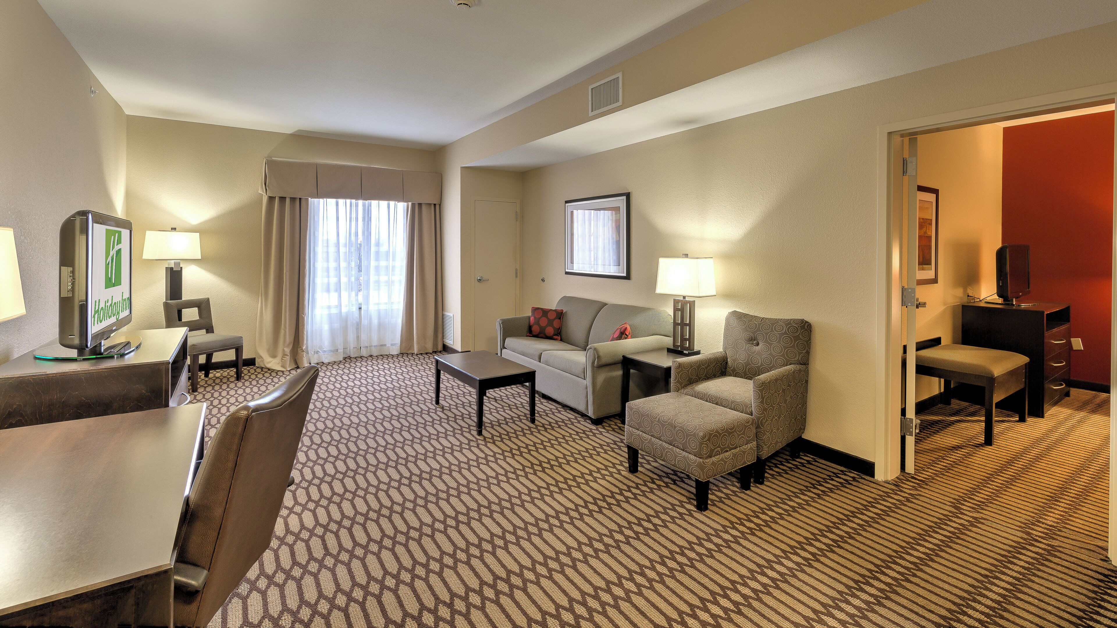 Habitación de hotel con escritorio, sofá, sillón, televisor y lámpara.
