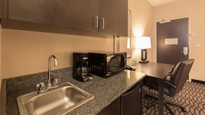 A hotel kitchenette with a sink, a coffee maker, a microwave, and a table with a chair.