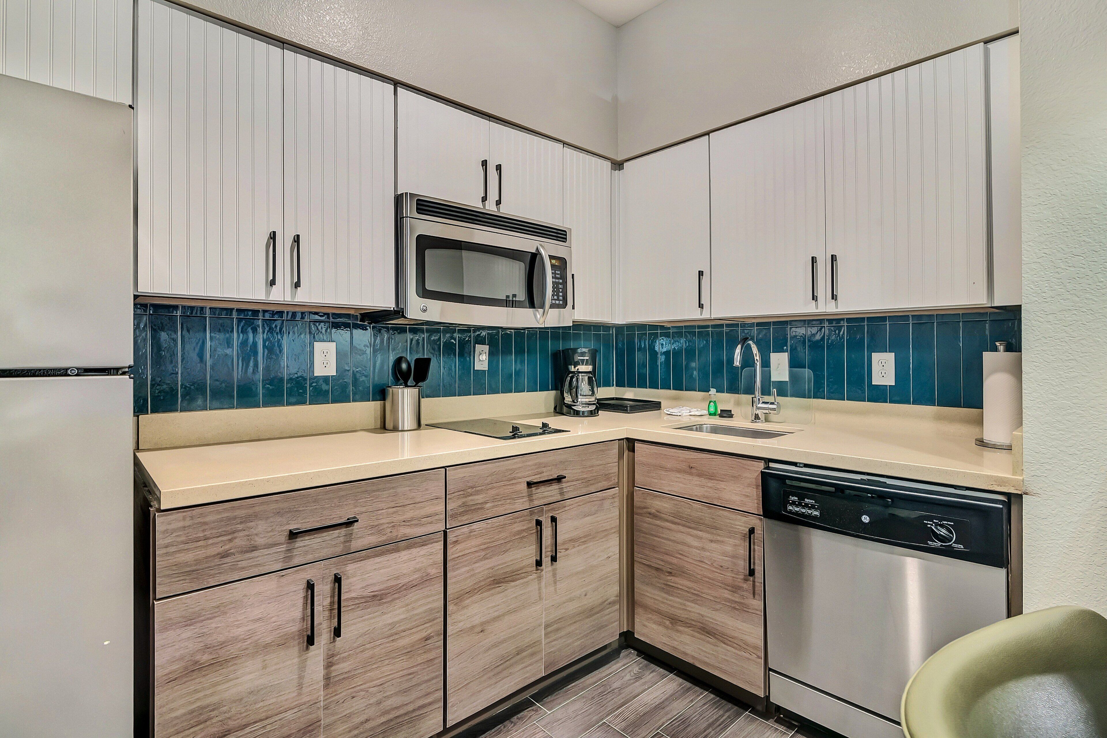 A compact kitchen with white cabinets, a stainless steel microwave, a coffee maker, and a dishwasher.