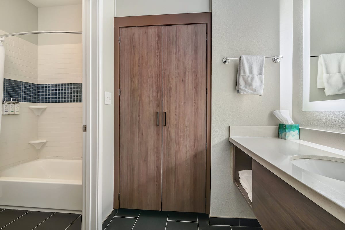 Un baño con puerta de madera, una bañera blanca, un lavabo blanco y un espejo.