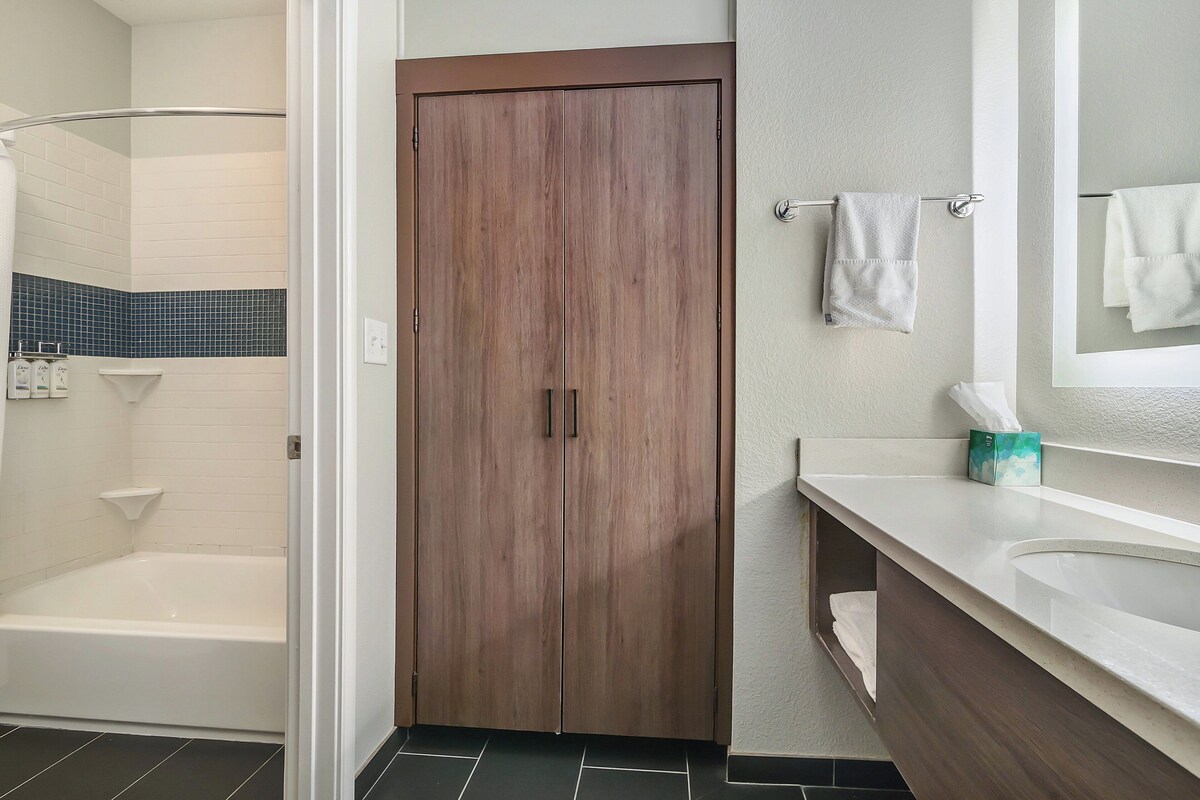 A bathroom with a wooden door, a white bathtub, a white sink, and a mirror.