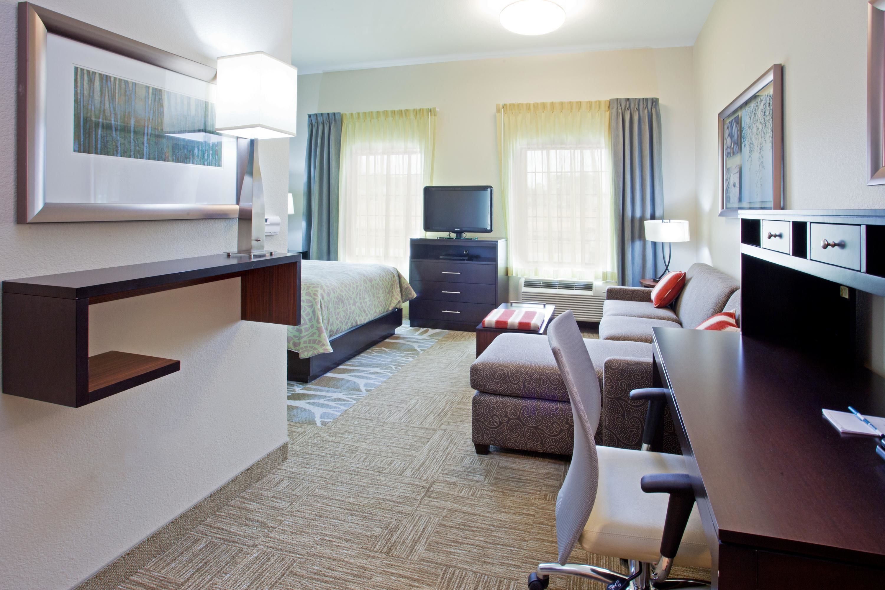 Quarto de hotel com cama, escrivaninha, cadeira, televisão e cômoda.