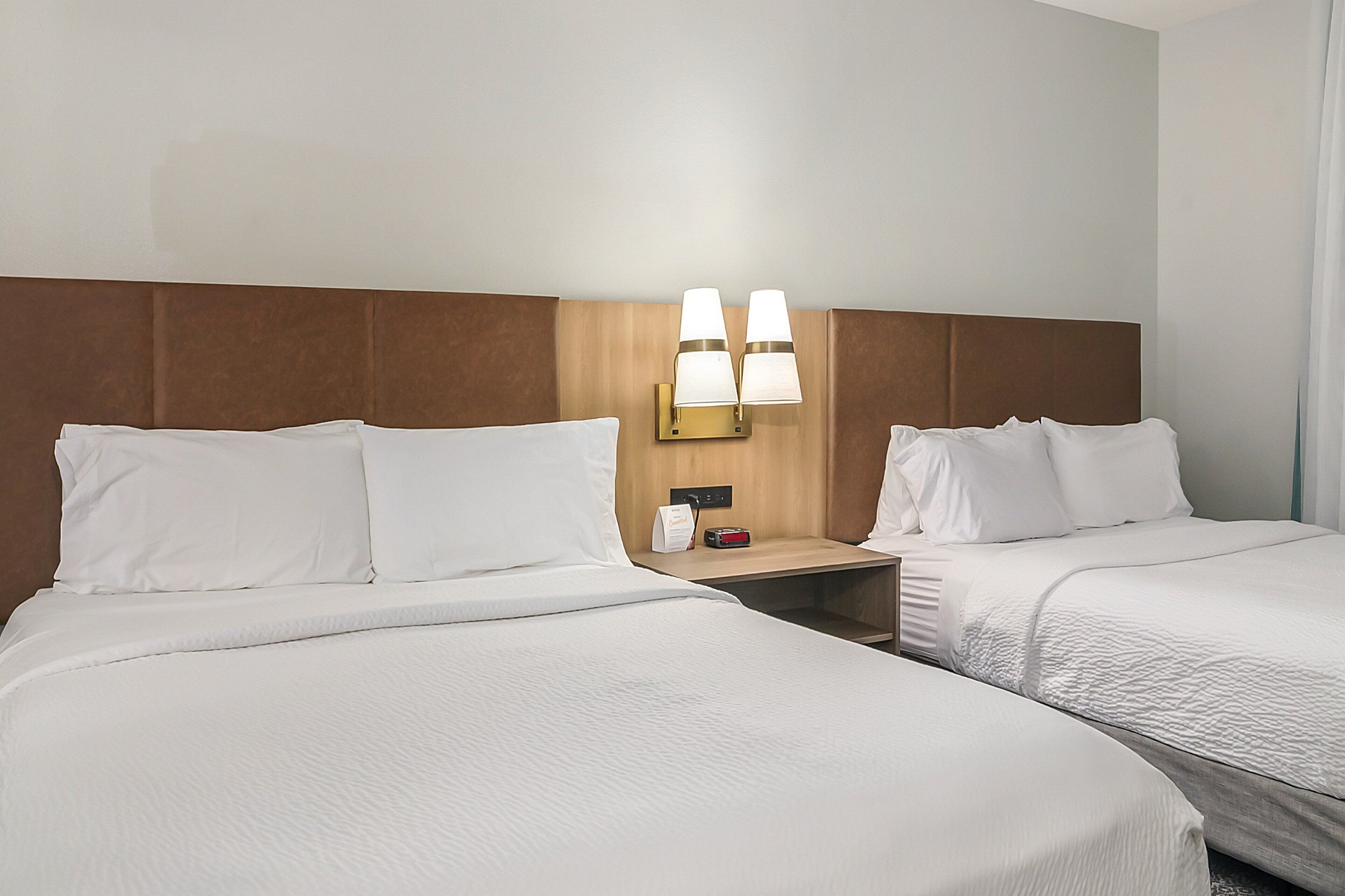 Een hotelkamer met twee bedden, een houten hoofdbord en een nachtkastje met een lamp.