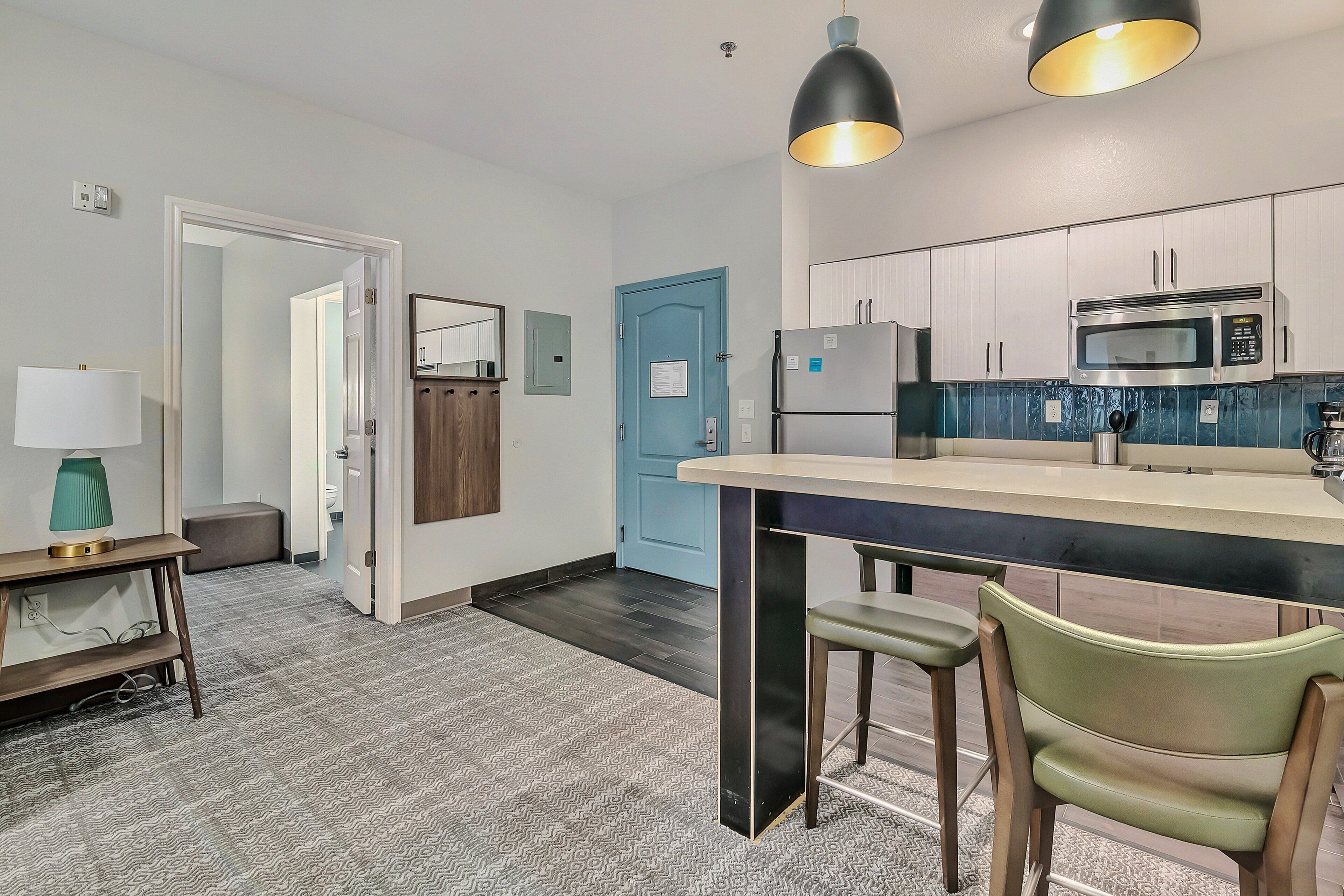 A modern kitchen with a central island, stainless steel appliances, and a blue door.