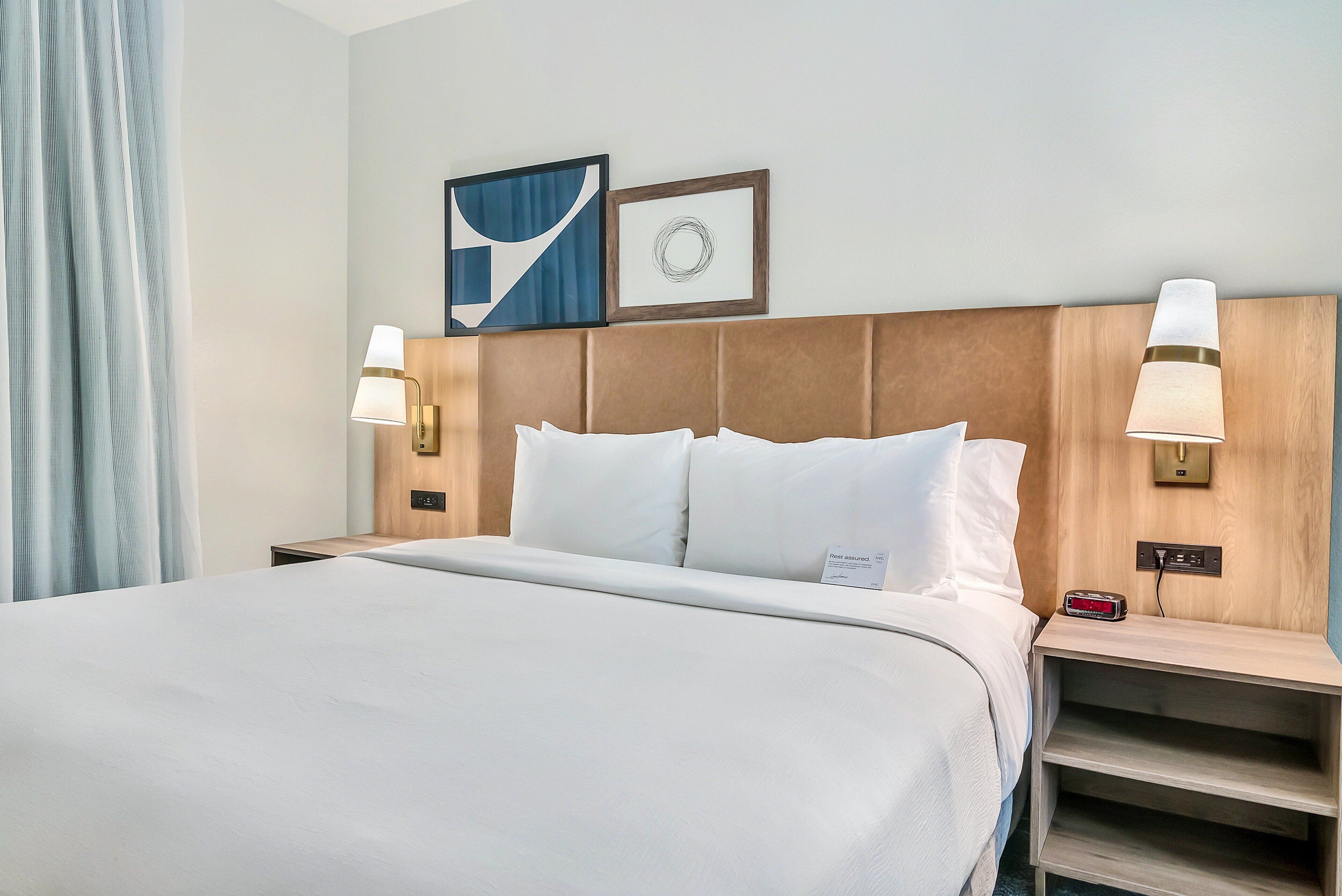 Una habitación de hotel con una cama grande, dos lámparas de noche, una mesita de noche y un reloj en la pared.