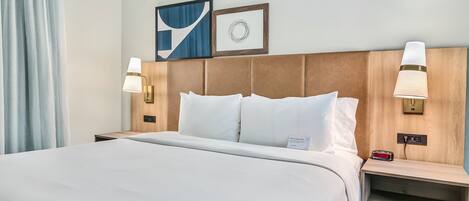 Una habitación de hotel con una cama grande, dos lámparas de noche, una mesita de noche y un reloj en la pared.