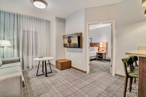 Habitación de hotel con sofá, una mesita, un reposapiés marrón, un cuadro de un toro y vista a otra habitación con cama y mesita de noche.